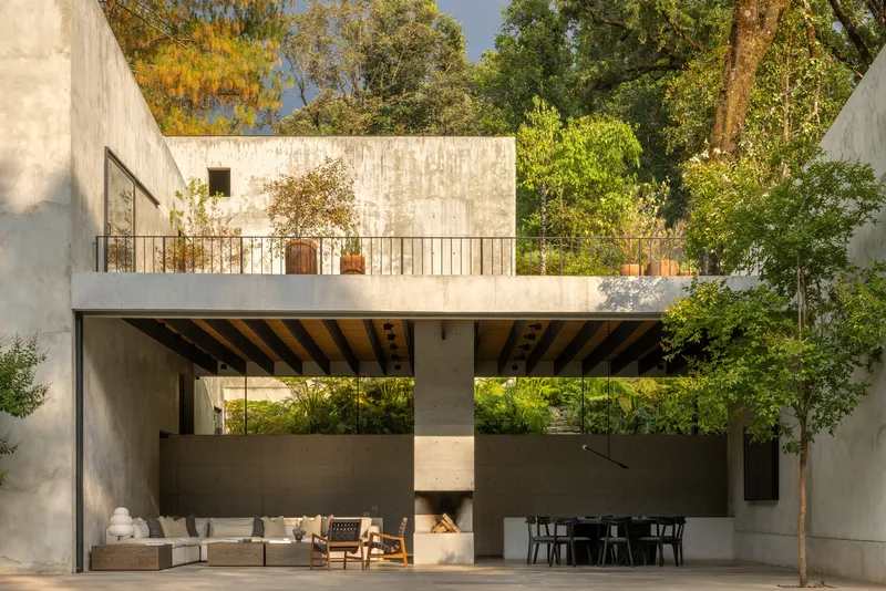 Double-height outdoor terrace with concrete fireplace and exposed beam ceiling beneath upper-level balcony