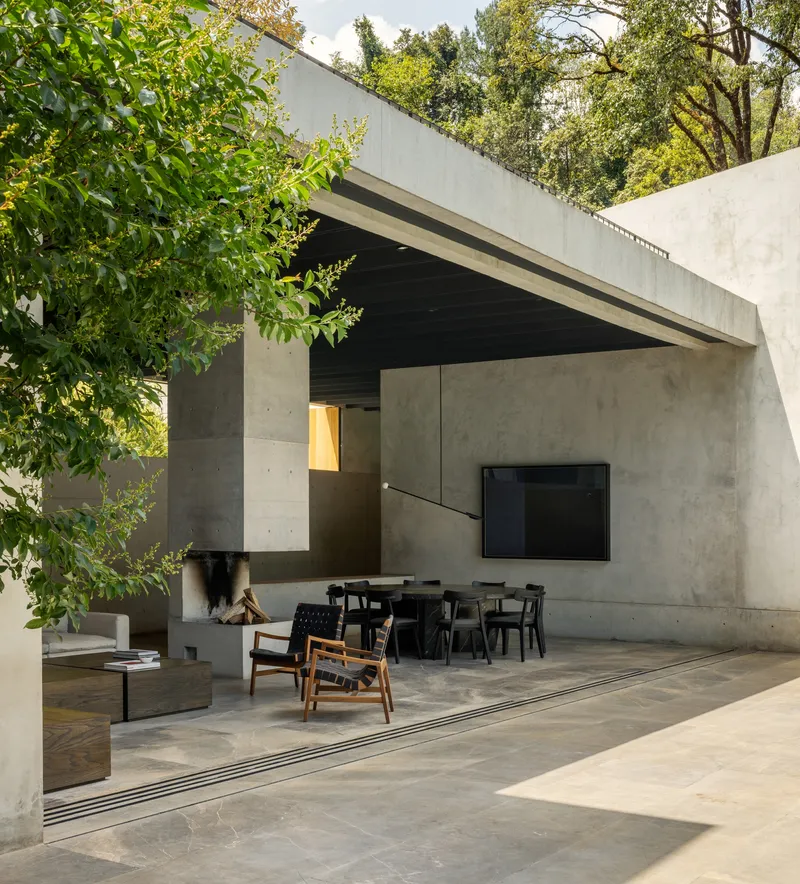 Covered outdoor living space with cantilevered concrete roof and tree branches framing the stone flooring