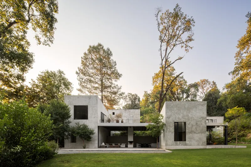 Garden view of the concrete volumes with open ground floor terrace framed by mature trees