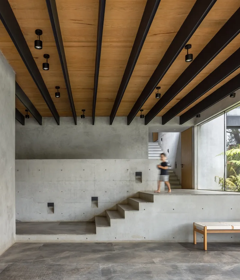 Double-height concrete stair with figure ascending beneath exposed timber and steel beam ceiling