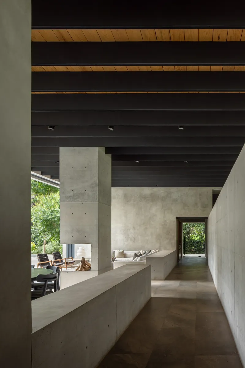 Interior corridor with concrete bench overlooking lawn through opening beneath layered timber and steel beams
