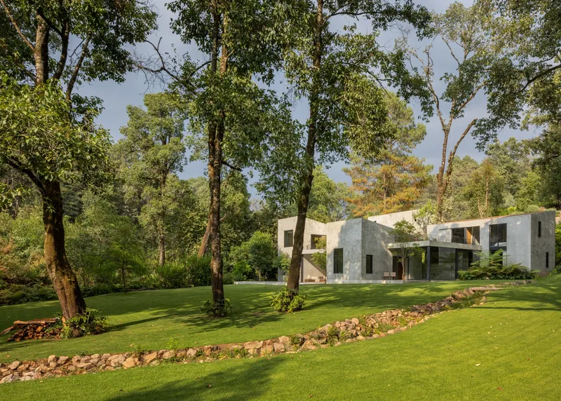 Rear elevation of concrete volumes on sloped lawn with curved stone border and mature trees
