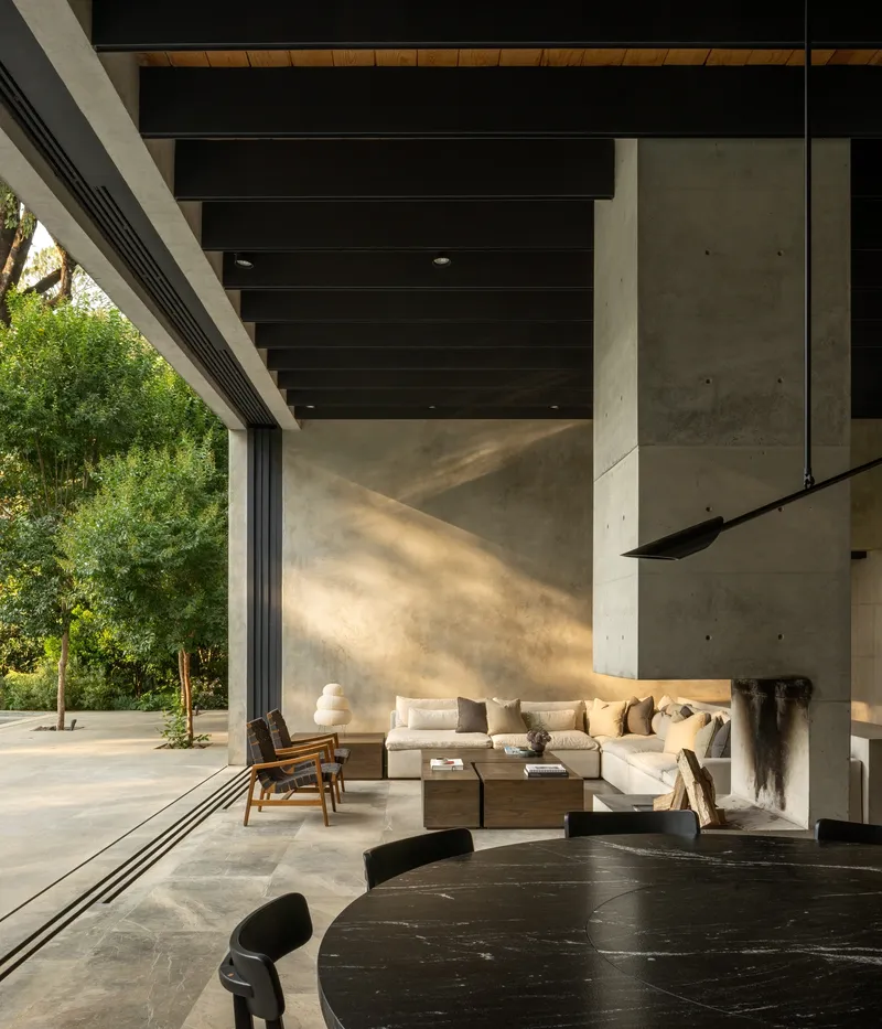 Open living space with full-height glazing, concrete fireplace and warm afternoon light across polished stone floor