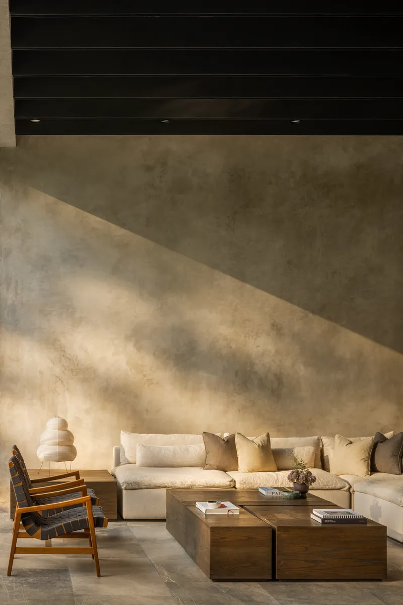 Concrete wall with dappled shadows cast across its surface above a seating arrangement with timber tables