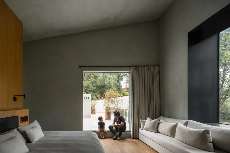 Bedroom with polished concrete walls and two figures seated by the glazed opening to the courtyard