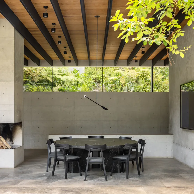Dining area with exposed timber ceiling beams and clerestory windows framing a dense planted wall