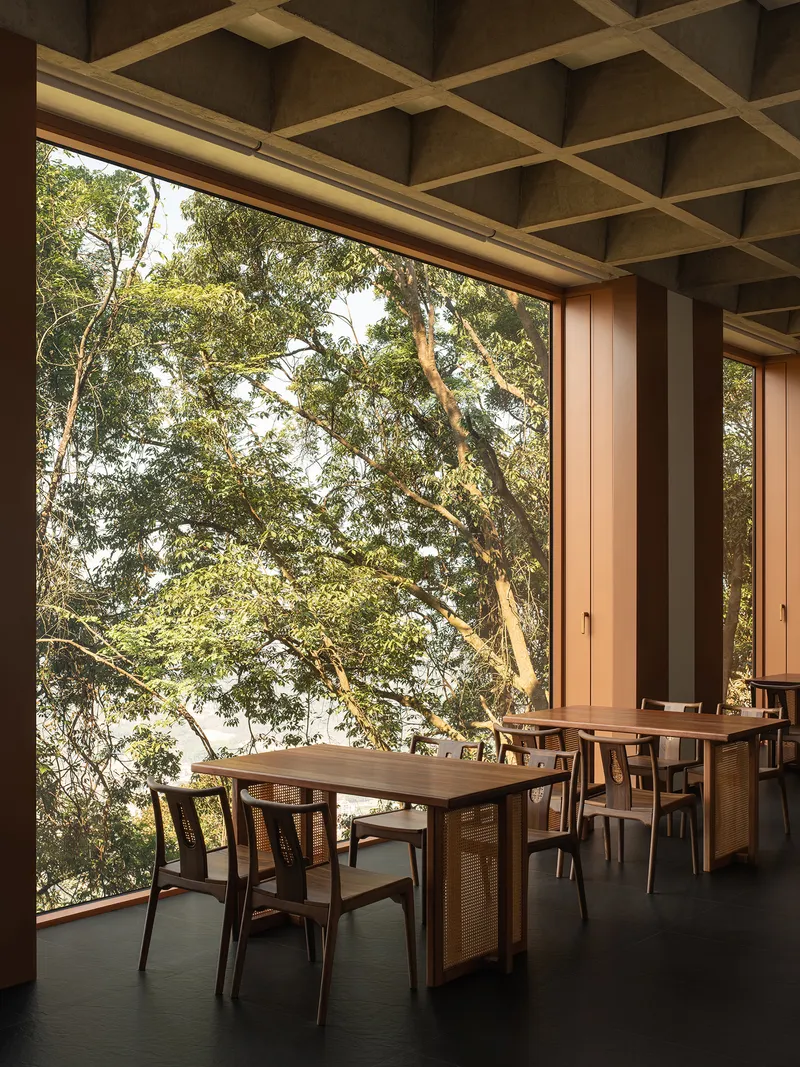 Dining terrace with coffered ceiling and floor-to-ceiling glazing opening onto a tree canopy