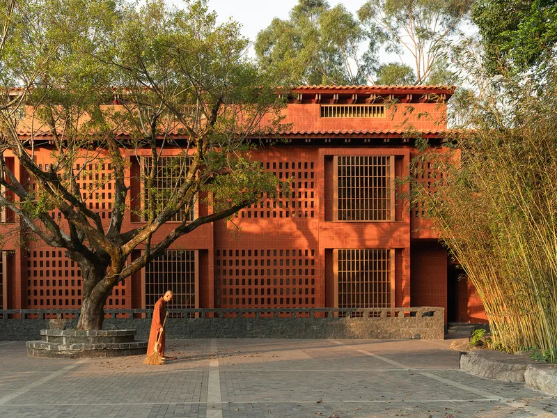 Red brick facade with lattice openings and grid windows under an established tree at golden hour