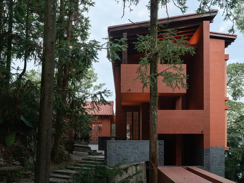 Multi-level red brick volume with exposed timber roof framing rising through tall pine trees
