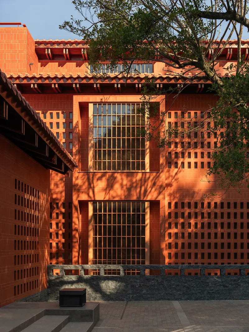 Courtyard facade showing paired grid windows framed by perforated red brickwork and tree shadows