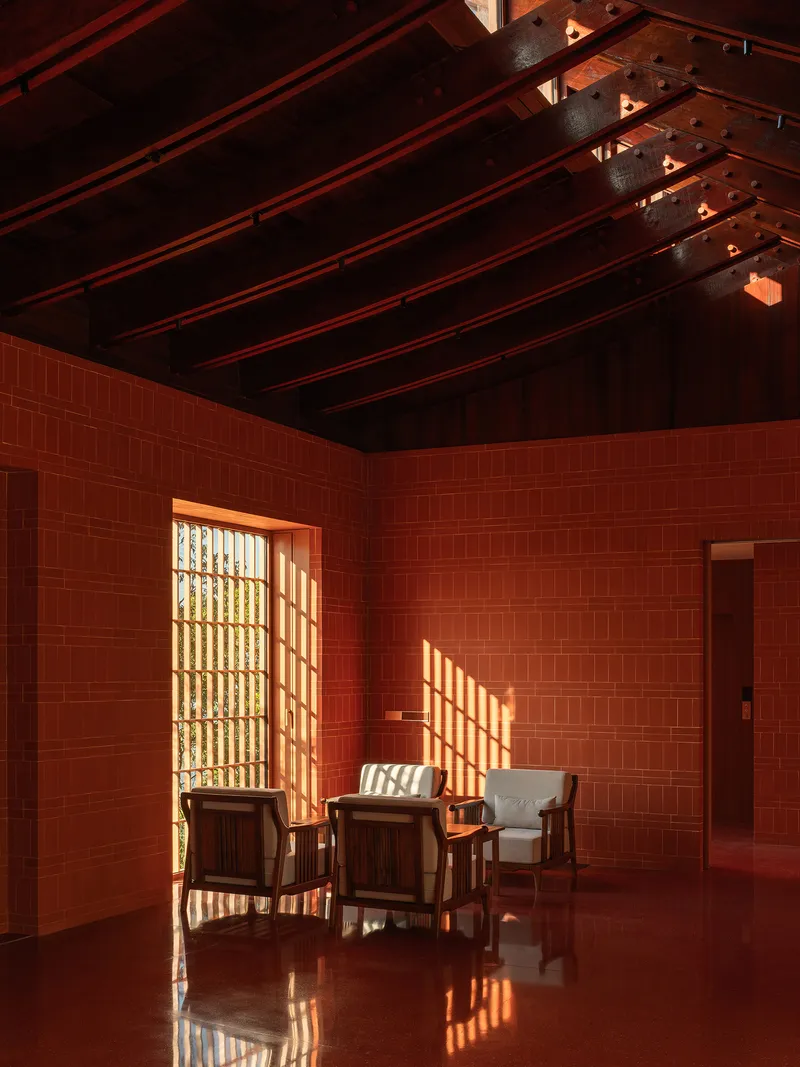 Interior room with red tile walls and exposed timber ceiling beams casting patterned light across seating