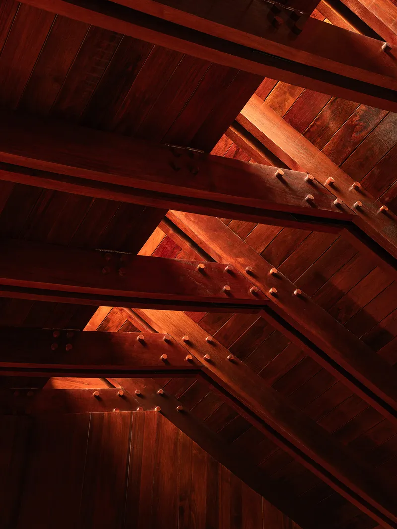 Interior view of exposed timber rafters and diagonal bracing with warm afternoon light filtering through