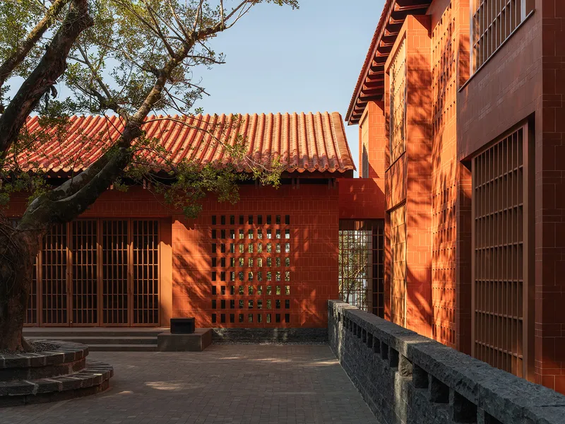 Courtyard with perforated red brick facades, clay tile roofs and a mature tree casting shadows
