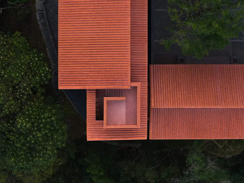 Aerial view of clay tile roofs with a central courtyard opening surrounded by forest canopy