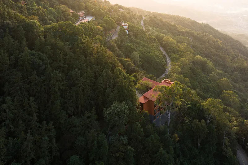 Drone view of red tile roofs nestled into a forested hillside at golden hour