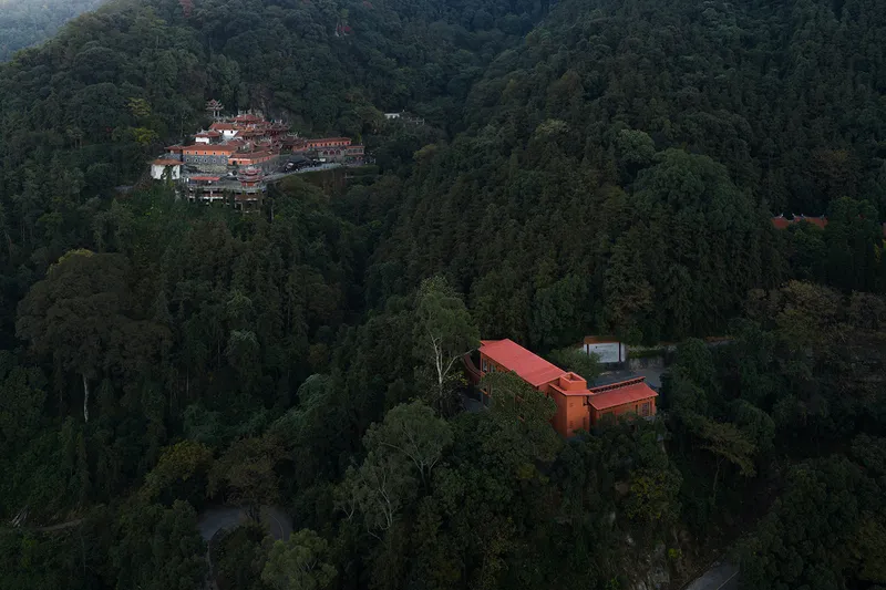 Aerial view of the red-roofed volumes nestled in dense forest at dusk