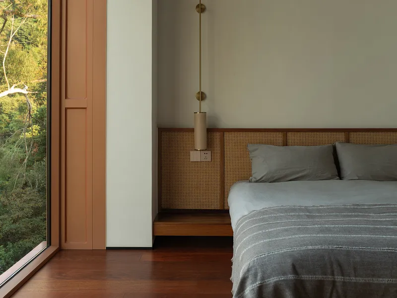 Bedroom with cane-paneled headboard wall and pendant light beside a full-height glazed door
