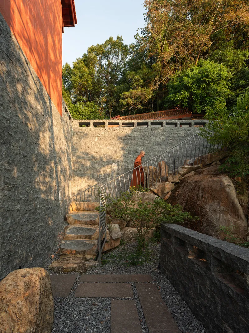 Exterior stone stair with metal railing ascending beside natural boulders and retaining walls at sunset