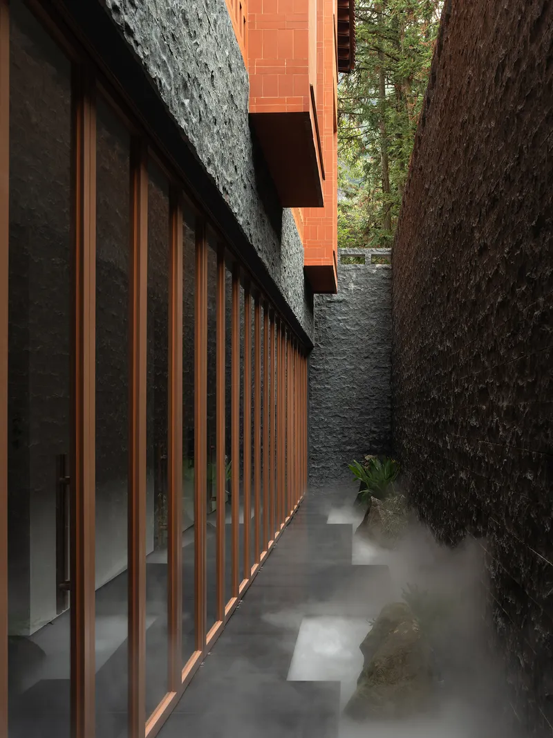 Narrow walkway with timber slat facade and stacked stone walls framed by tree trunks