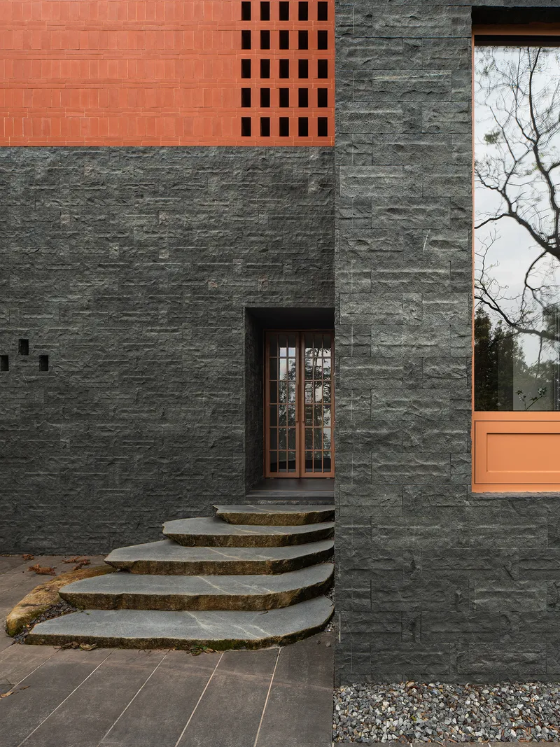 Fanned stone entry steps leading to glazed door set in dark stacked stone facade with terracotta accents
