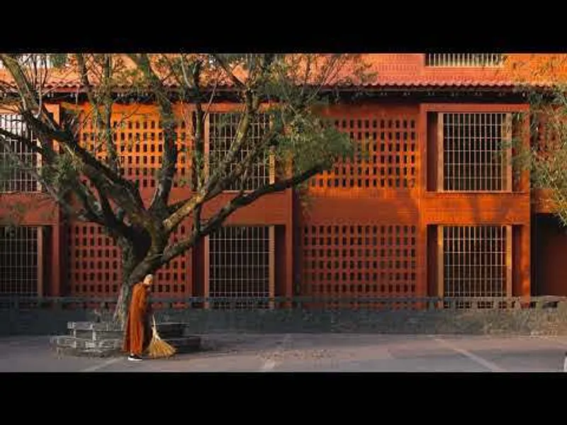 Terracotta lattice brick facade with regular window openings and a tree in the foreground at dusk