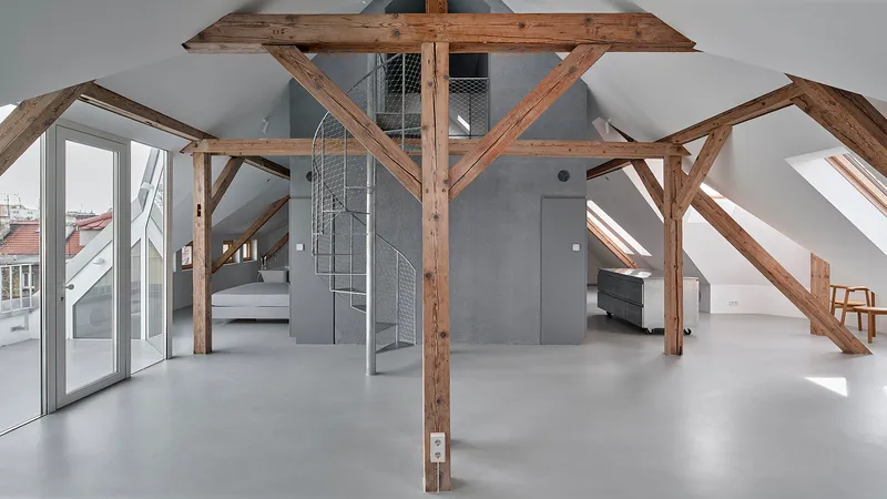 Attic interior with exposed timber trusses, wire mesh spiral staircase, and polished concrete floor under skylights