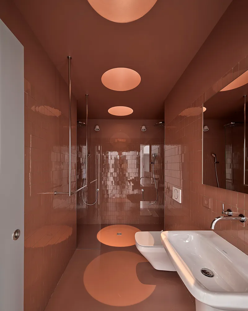 Terracotta-tiled bathroom with circular ceiling lights and glass shower enclosure under amber glow