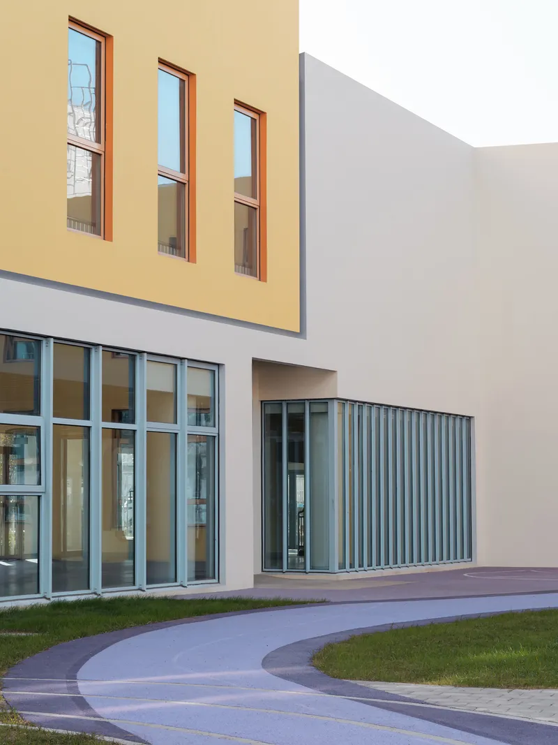 Ground-level view of the entry with glass curtain wall and vertical metal louvres beside a curved pathway