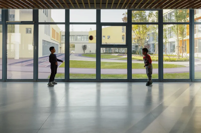 Interior corridor with floor-to-ceiling glazing and two children playing with a ball
