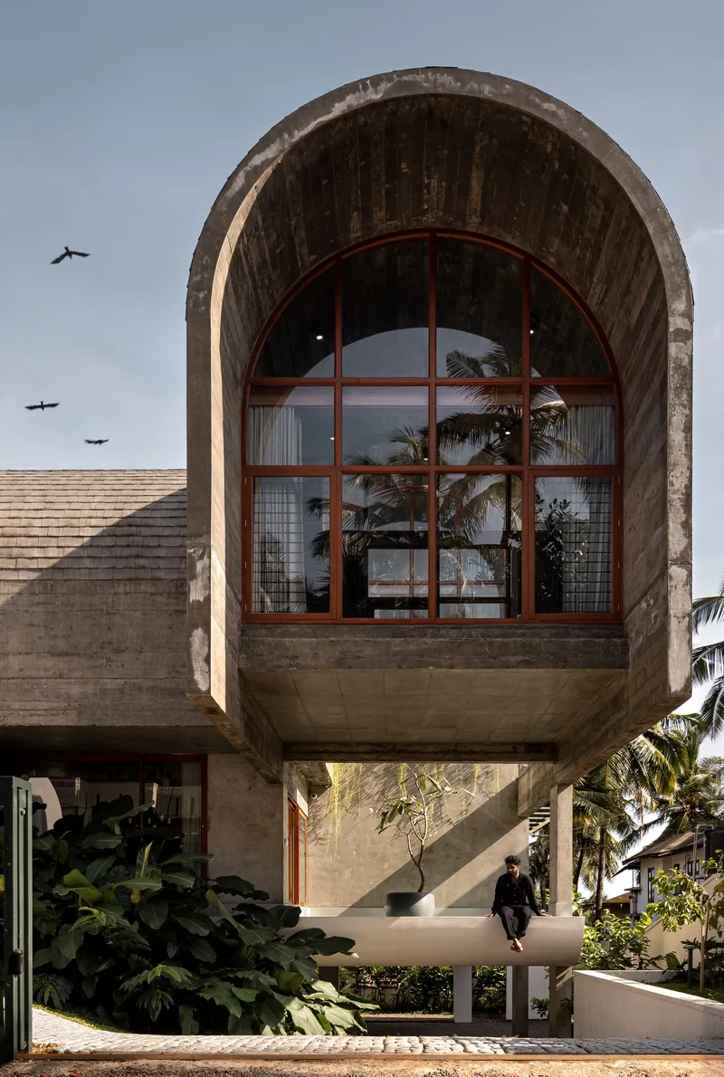 Barrel-vaulted concrete volume with arched timber-framed window and birds flying overhead at dusk