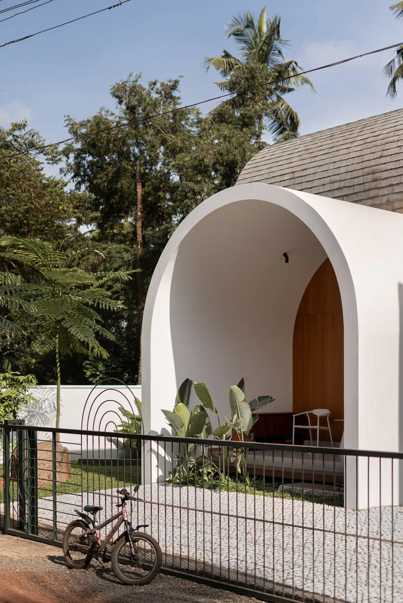 White barrel-vaulted pavilion opening to a courtyard with planted beds and a bicycle at the railing