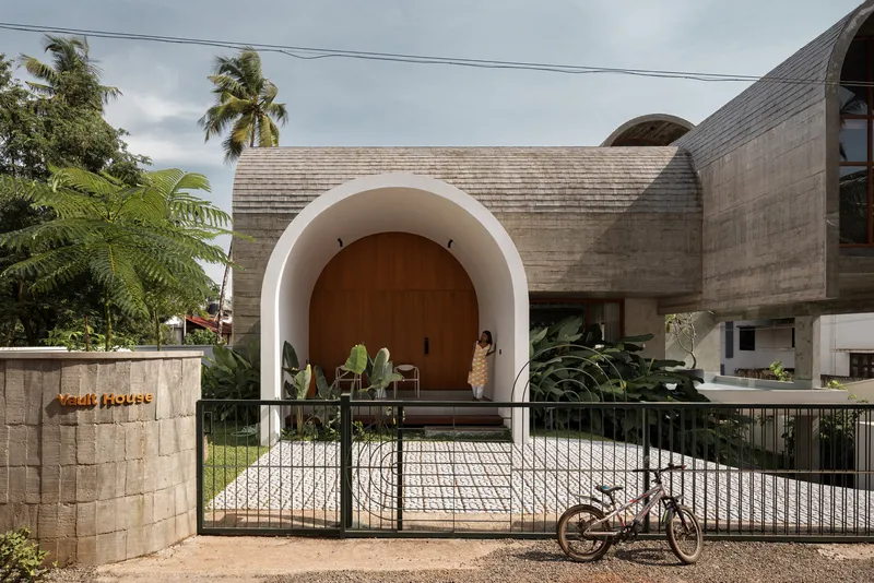 Arched entry portal with timber door and white stucco surround framed by a black metal gate
