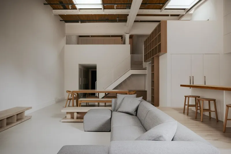 Double-height living space with exposed timber ceiling joists and skylights above a mezzanine with open shelving