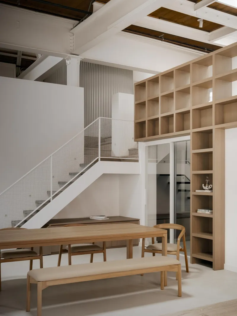 View of the white staircase with perforated metal balustrade beneath a floor-to-ceiling timber shelving wall