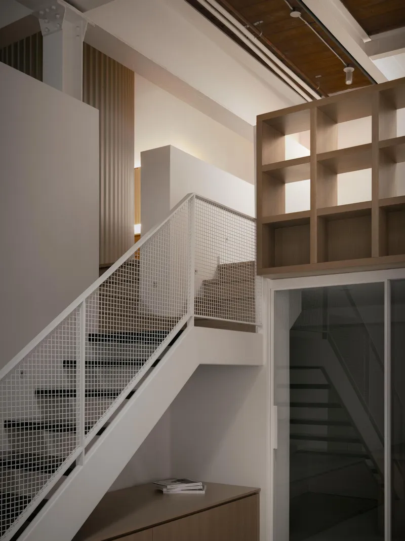 White staircase with mesh railing ascending past timber shelving and glazed doorway in double-height space