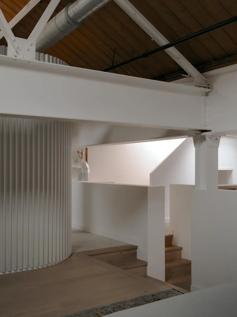 Timber staircase with white wall wrapping around curved vertical louver screen under exposed wood ceiling