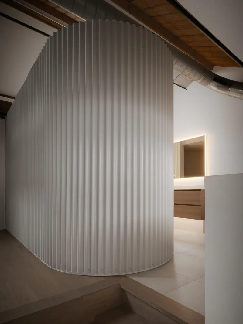 Curved white louver screen enclosing volume with glimpse of backlit timber cabinetry beyond
