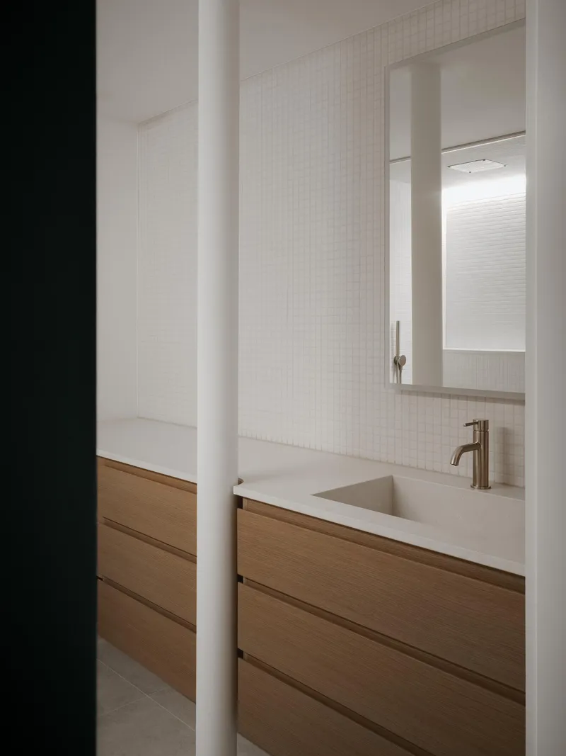 Bathroom vanity with oak drawer fronts and integrated sink viewed through a dark doorway