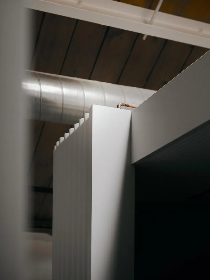 Angled interior corner showing fluted wall panel beside exposed ducting and timber ceiling planks