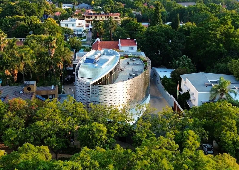 Aerial view of the curved perforated facade rising above a lush residential neighborhood with palm trees