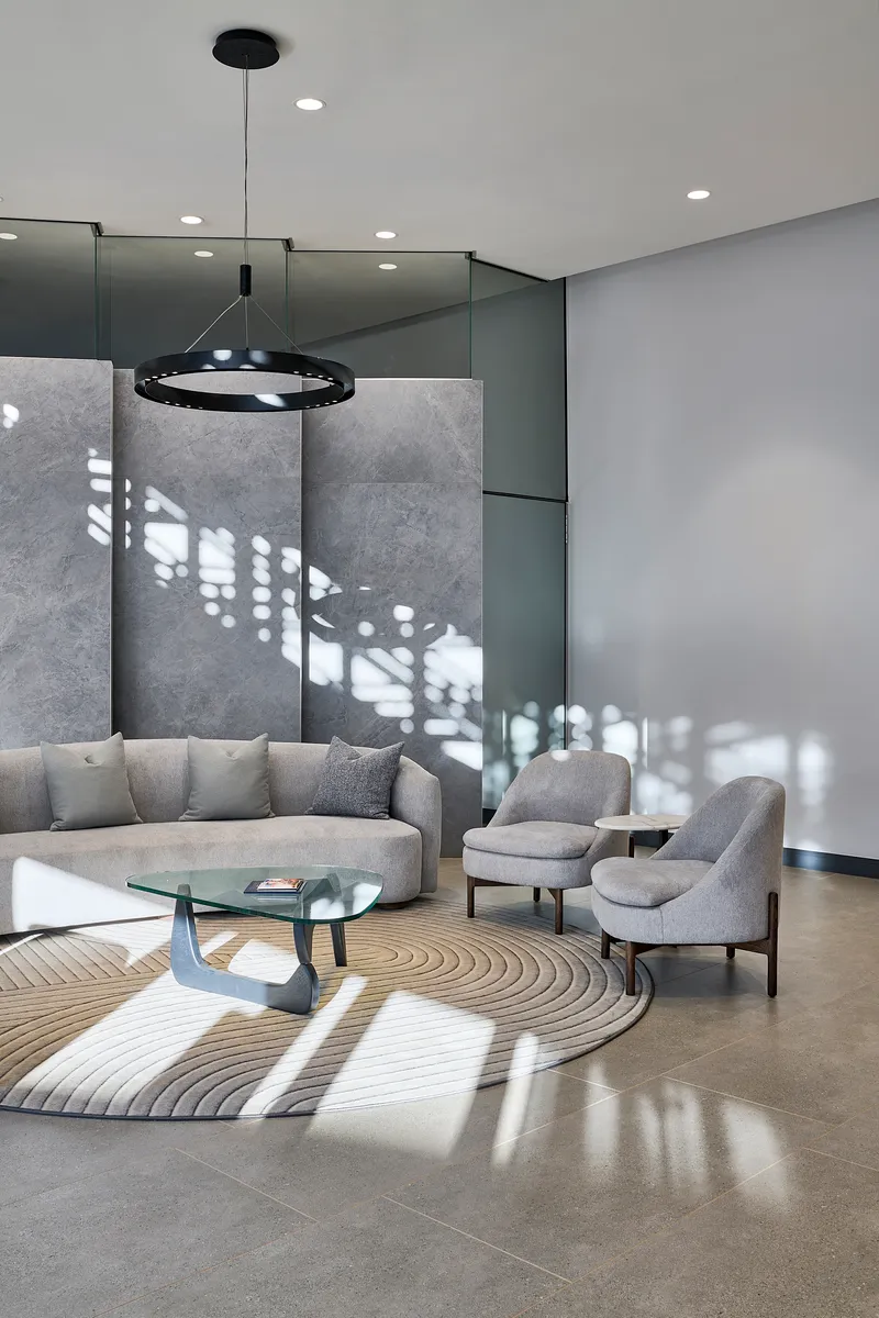Double-height lounge with filtered light casting geometric shadows across concrete panels and polished floor