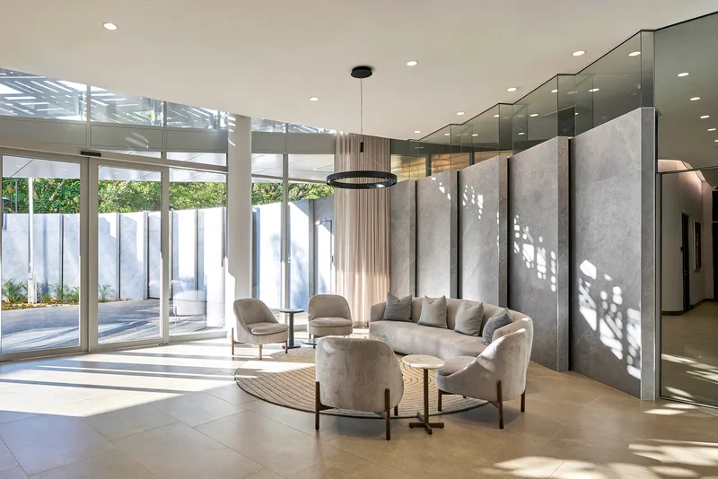 Interior seating area with floor-to-ceiling glazing overlooking courtyard and patterned light on concrete walls