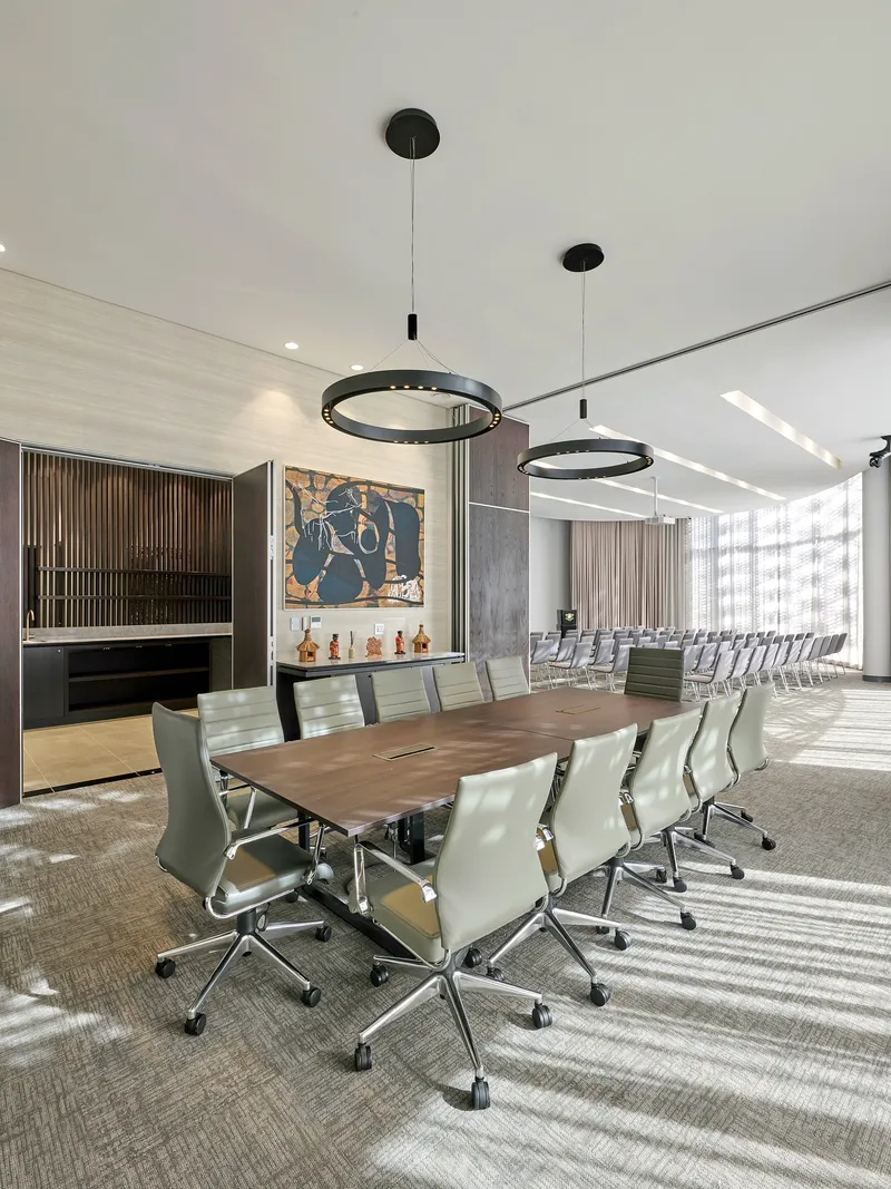 Conference room with long wooden table and white leather chairs beneath black circular pendant lights