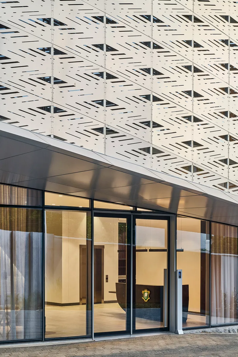 Ground floor entrance with black framed glazing beneath a white perforated panel facade at dusk