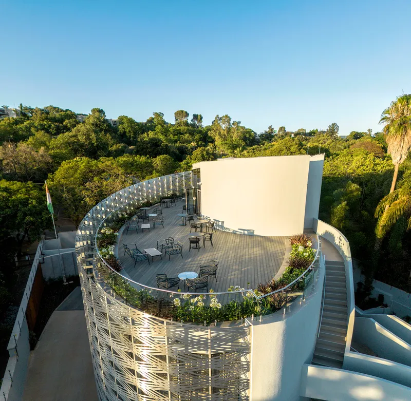 Aerial view of curved rooftop terrace with outdoor furniture and planted beds in late afternoon light