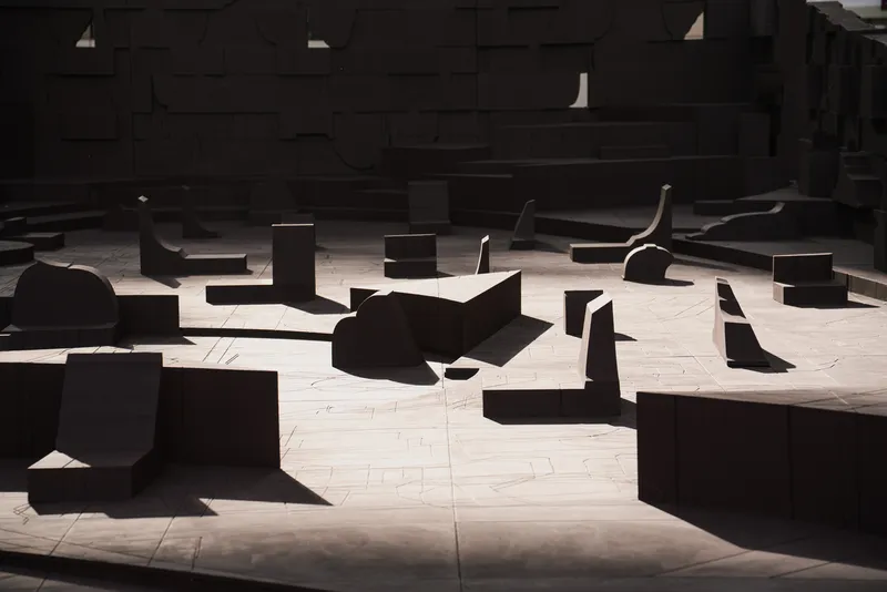 Sunlit plaza floor with silhouetted seating elements casting shadows across pale stone paving