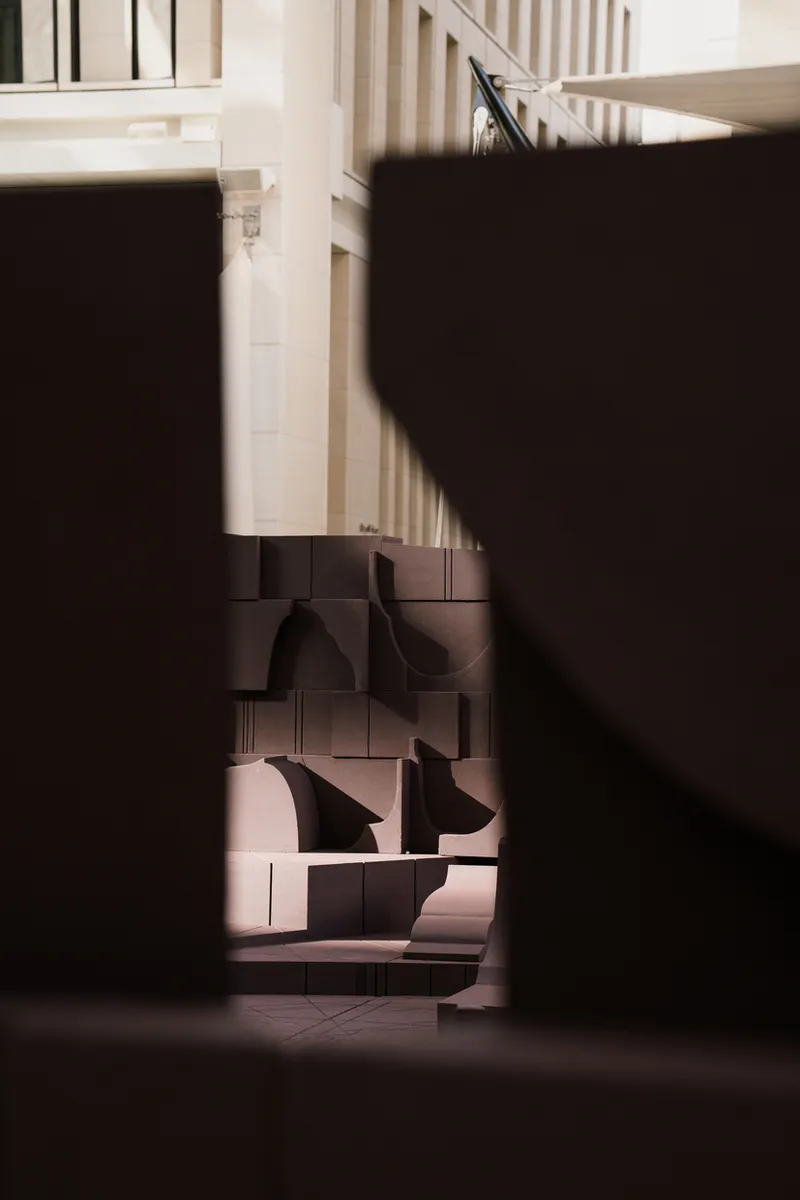 Shadowed view through dark sculptural forms with striped building facade visible in bright background