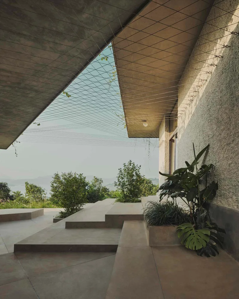 Covered terrace with folded concrete soffit and cable tensioning overlooking a landscape beyond planted beds