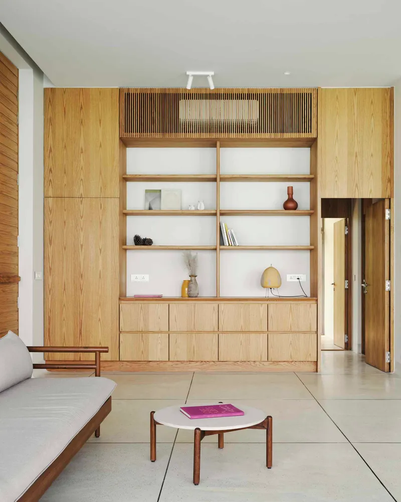 Floor-to-ceiling oak storage wall with integrated shelving and slatted ventilation panel in white-walled living space