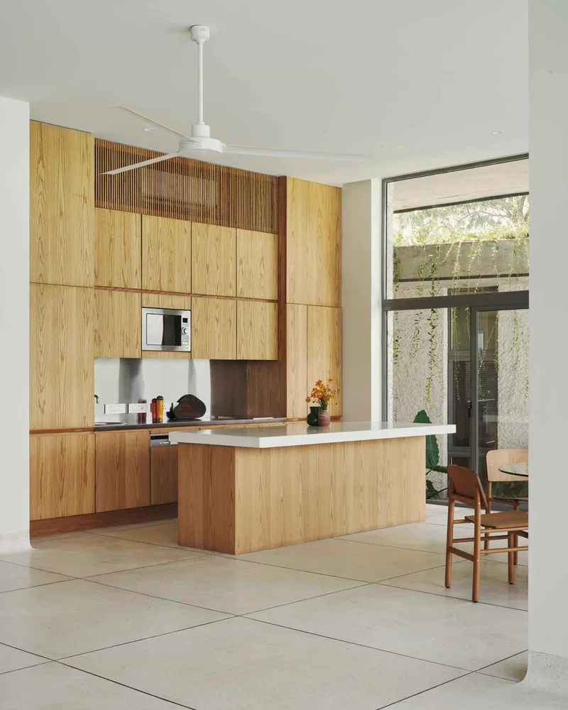 Open kitchen with oak island and cabinetry opening to planted courtyard through glazed corner doors